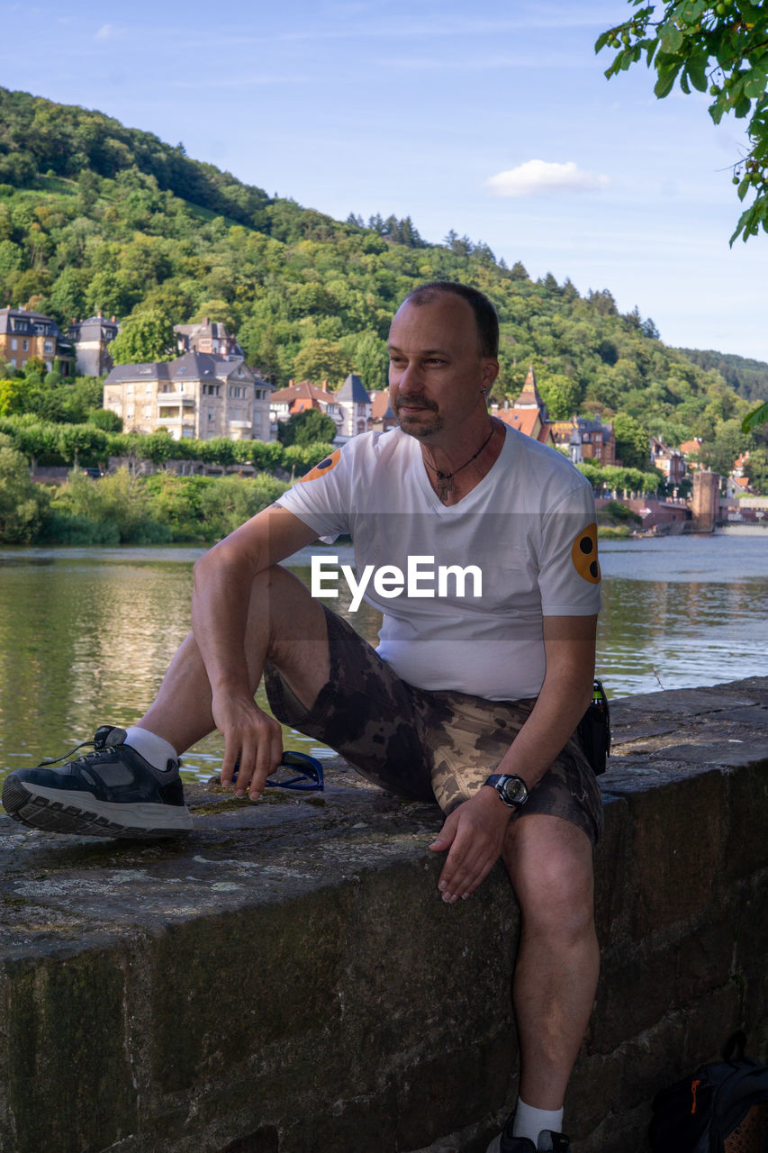 Full length of man sitting by lake against sky