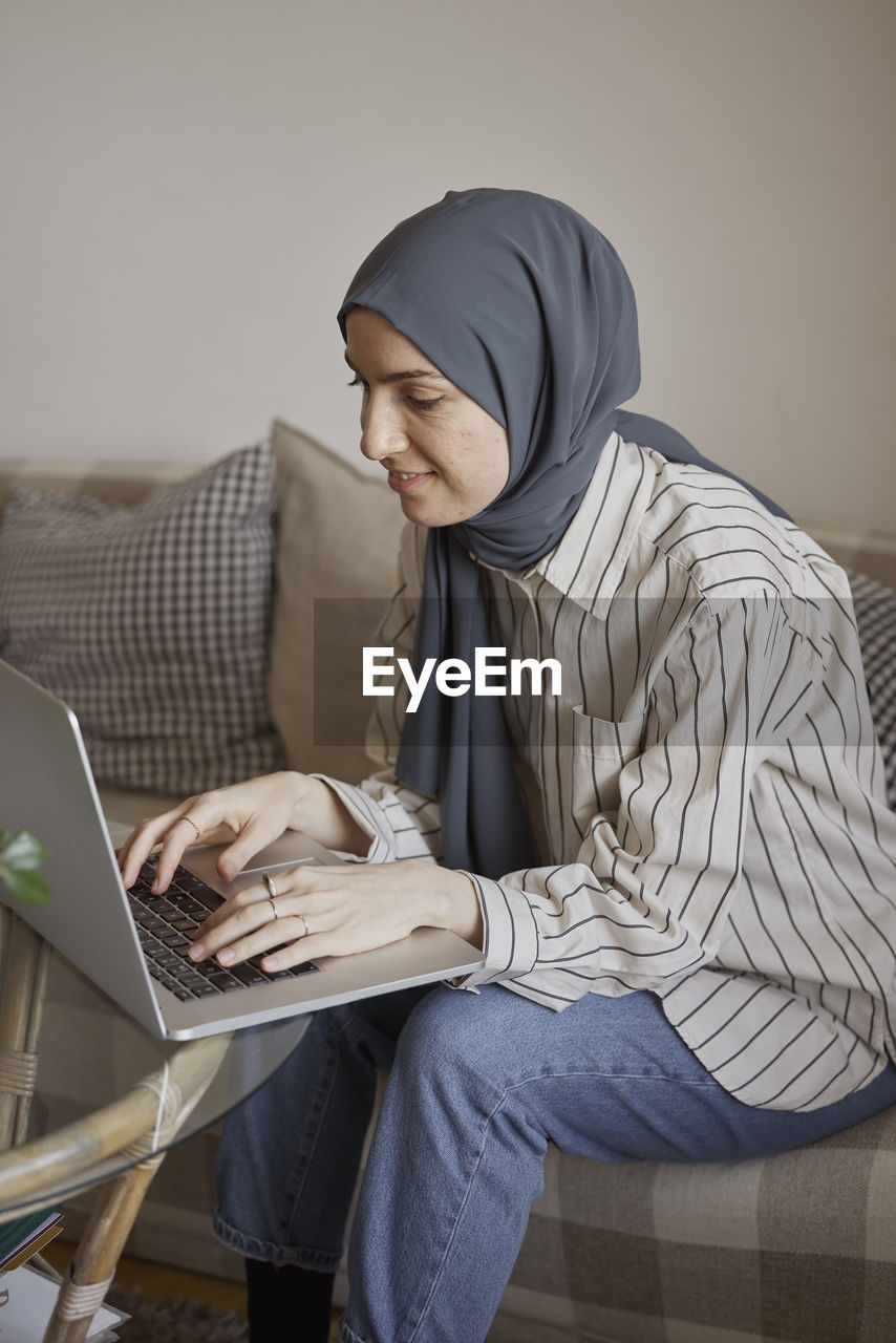 Young businesswoman typing on laptop while working from home in living room