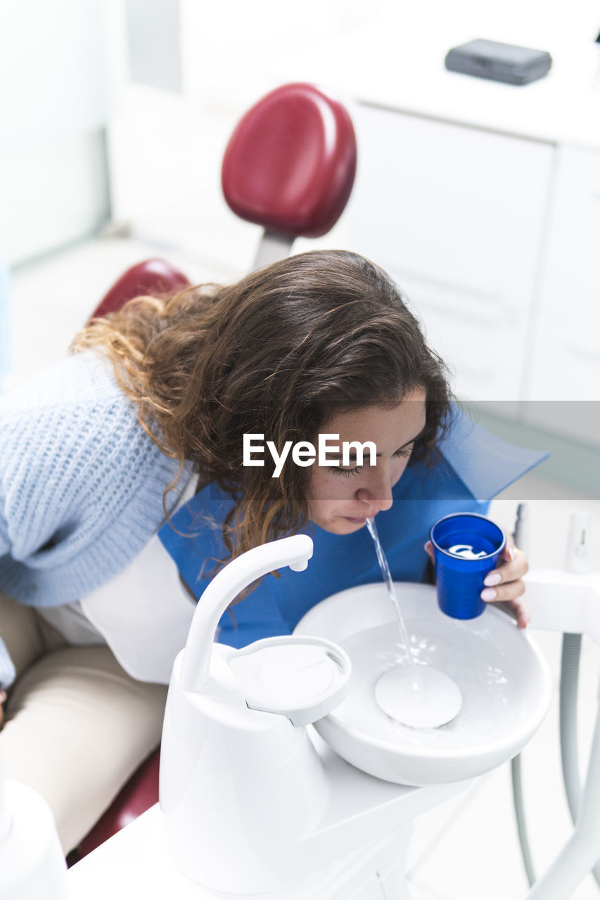 Woman spitting water in sink at dental clinic