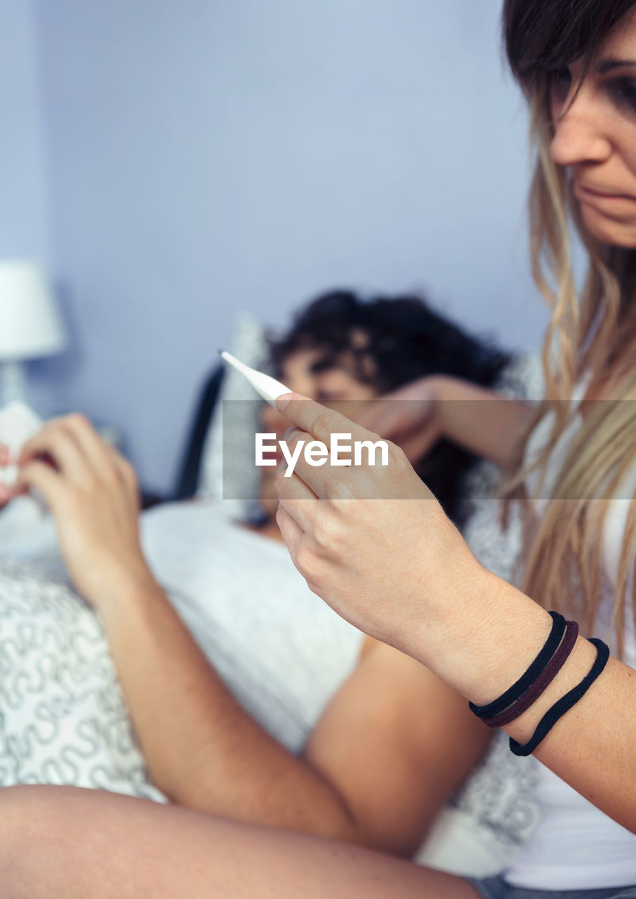 Girlfriend checking temperature of boyfriend with flu on bed