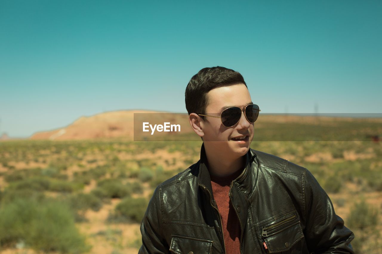 Close-up of smiling young man wearing sunglasses against clear sky