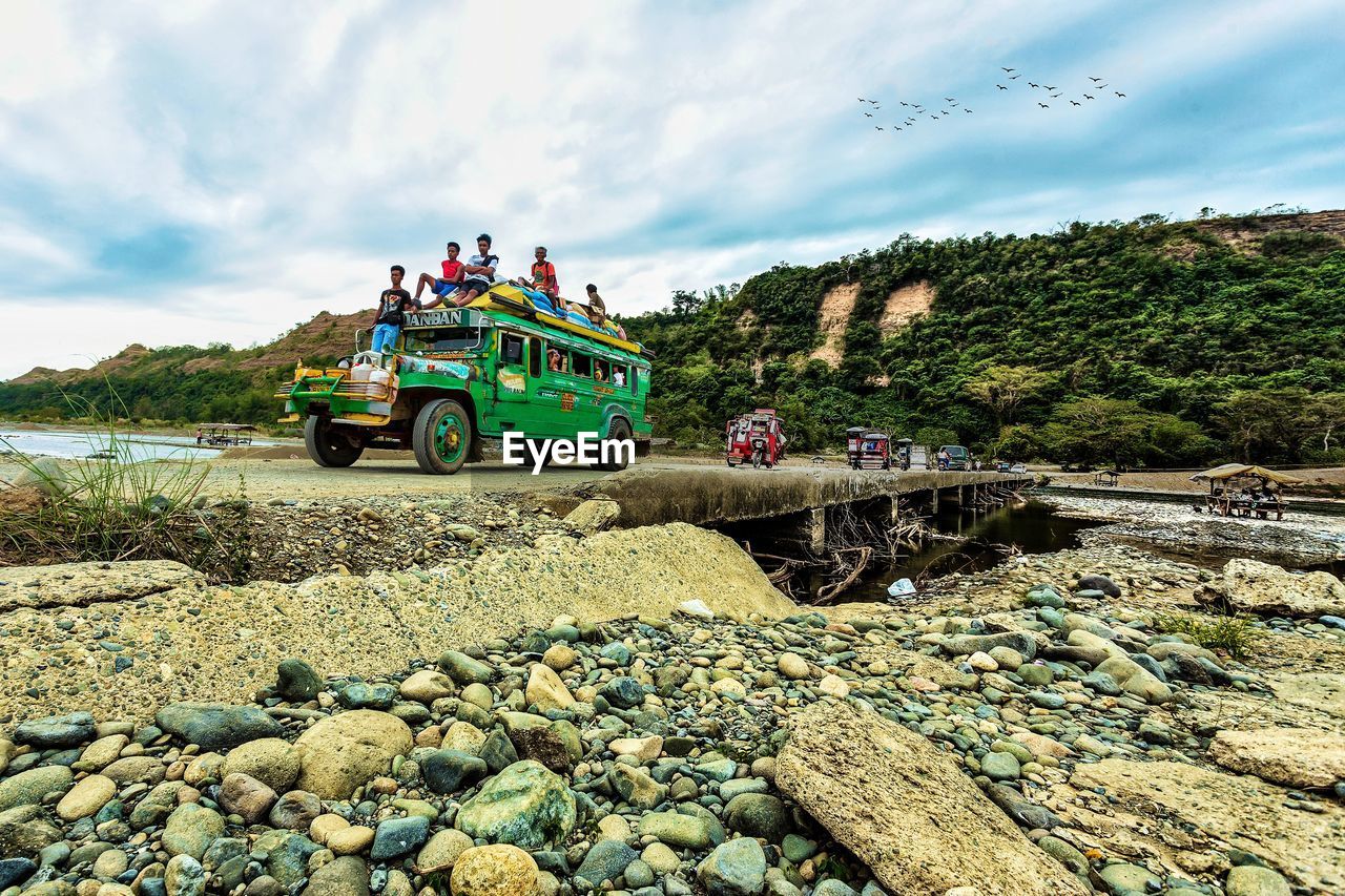 GROUP OF PEOPLE ON ROCKS BY ROAD