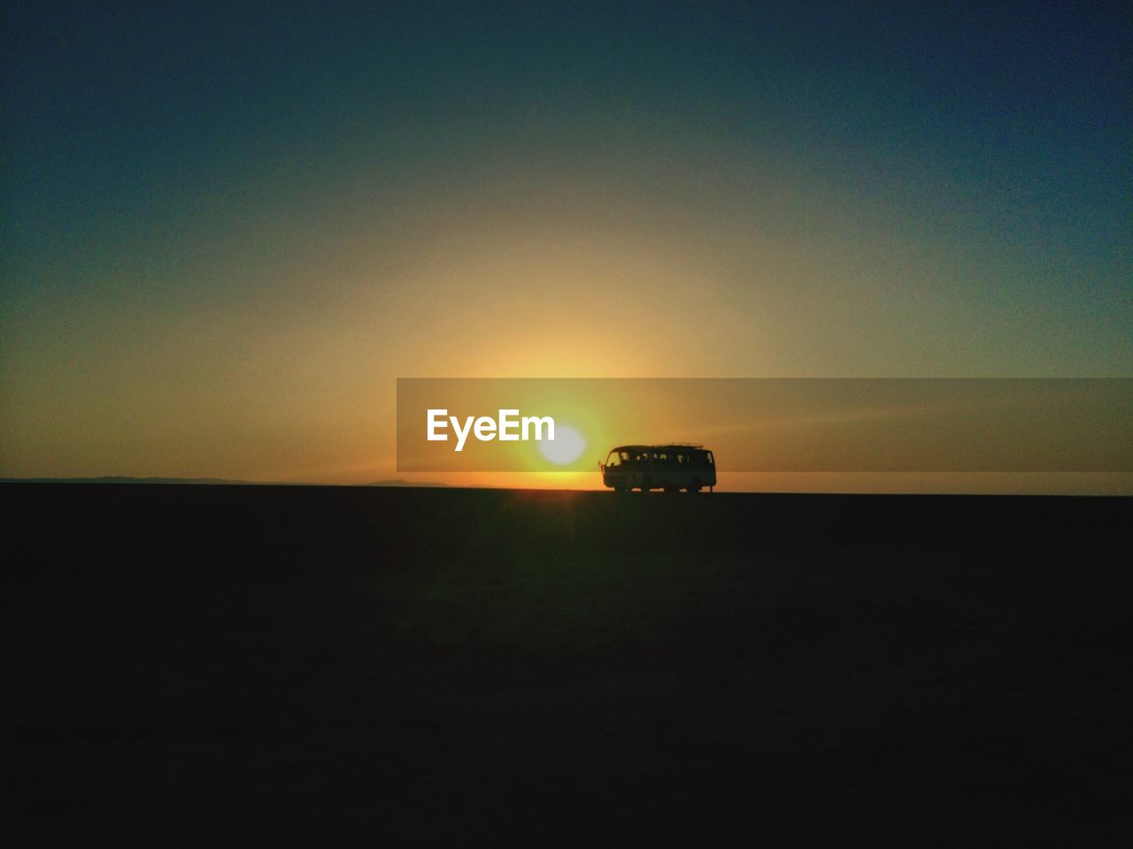 Idyllic shot of silhouette van on landscape against orange sunrise sky
