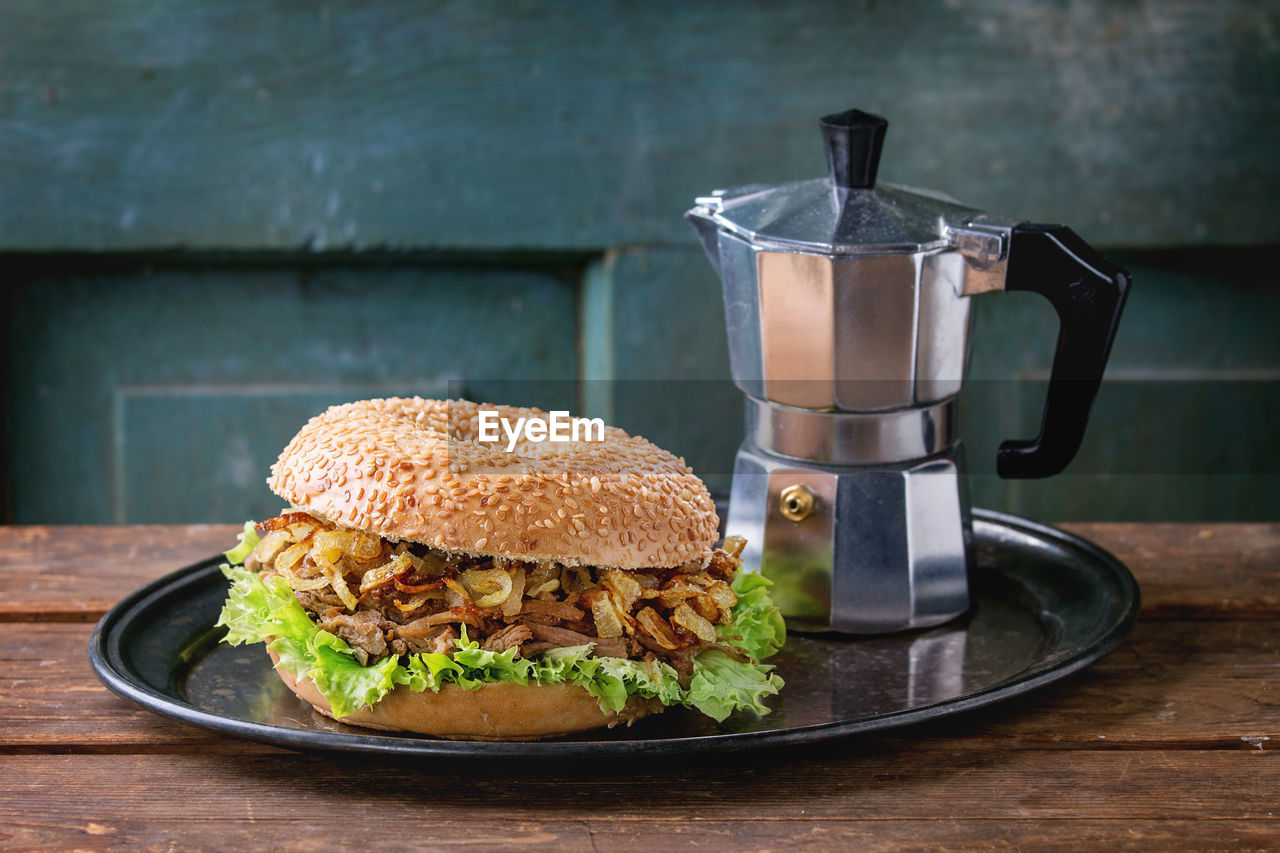 Close-up of burger and coffee maker in tray on wooden table
