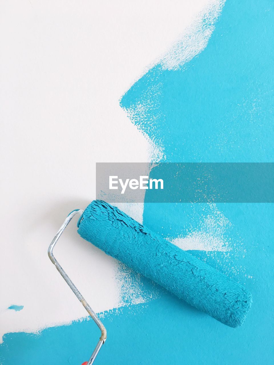 Close-up of paint roller with blue paint over white background