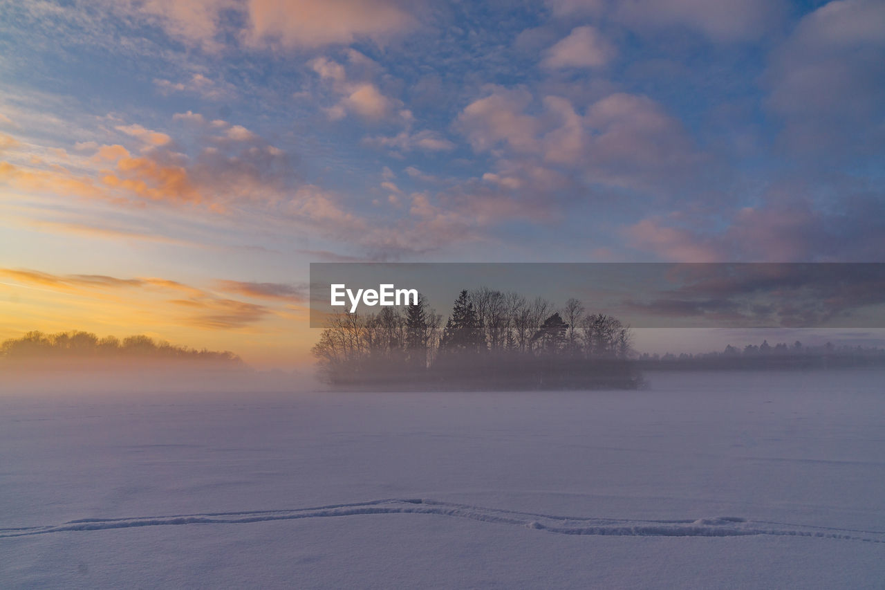 Scenic view of frozen landscape against sky at sunset