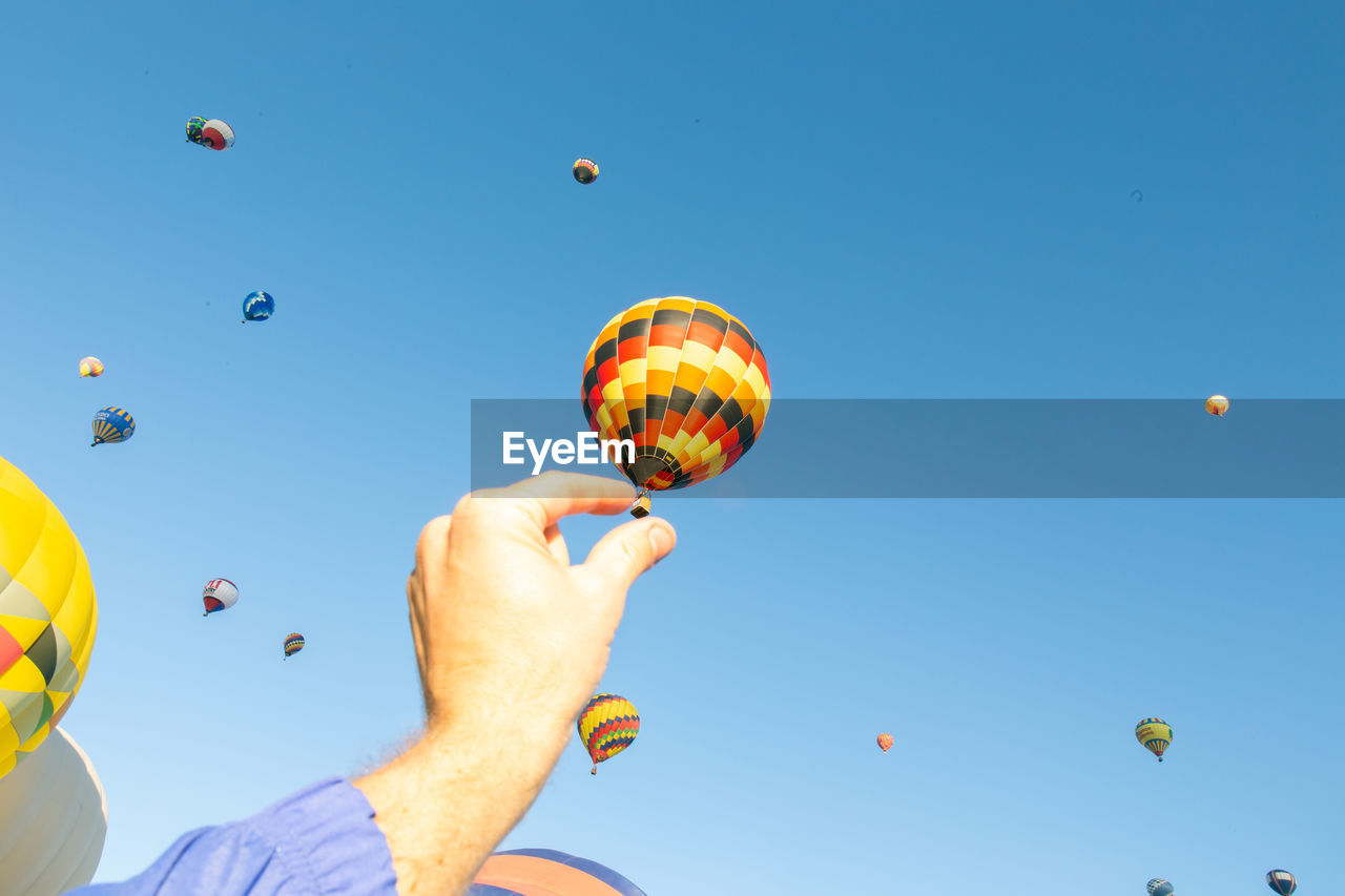 Optical illusion of cropped hand holding hot air balloons against sky