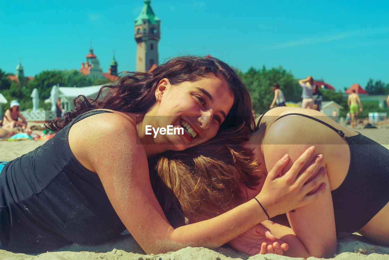 Cheerful friends lying on sand at beach during sunny day