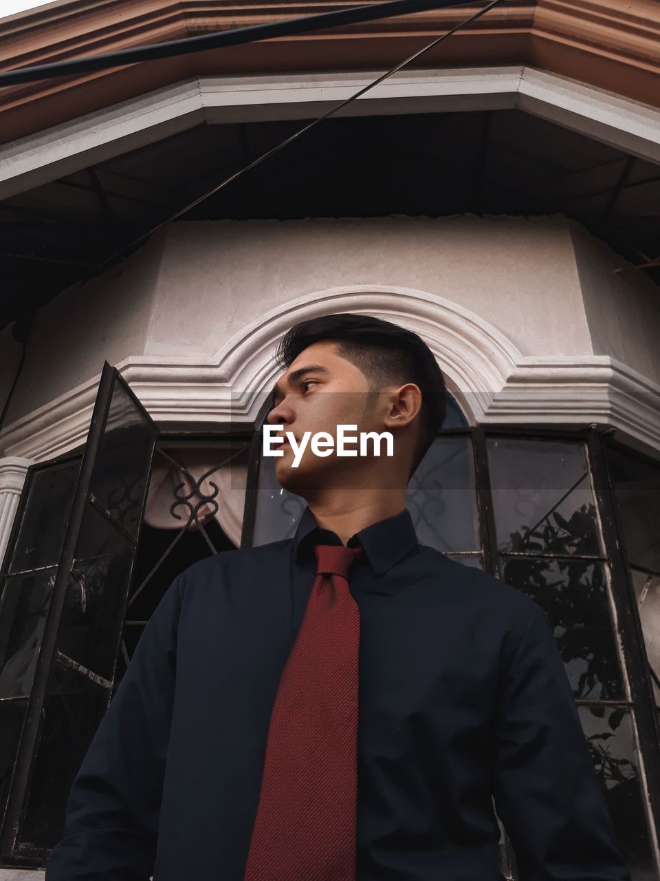 Low angle view of young man looking away while standing against building