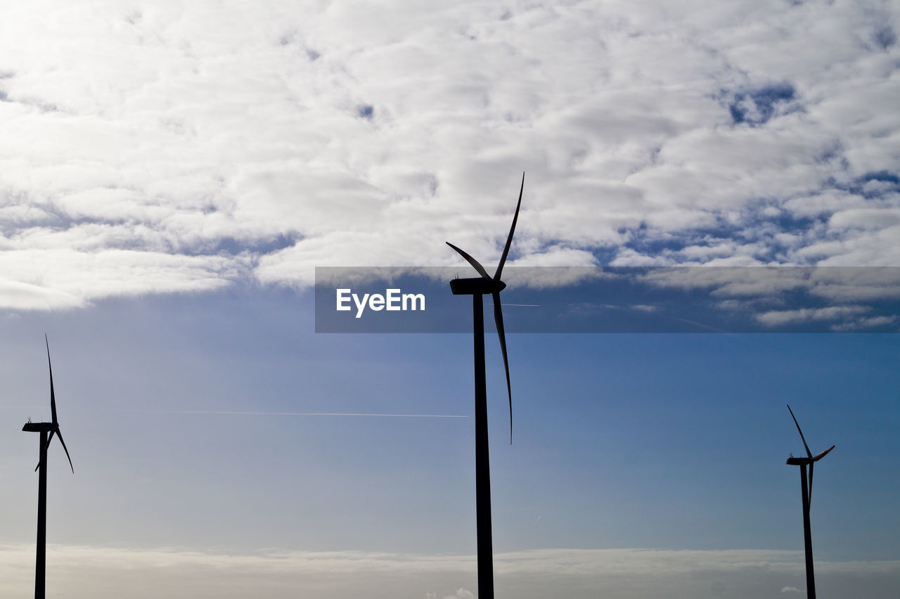 Low angle view of windmills against cloudy sky