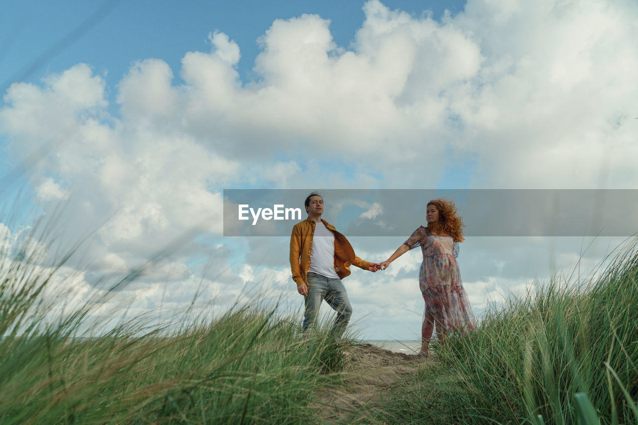Couple standing on grass against sky