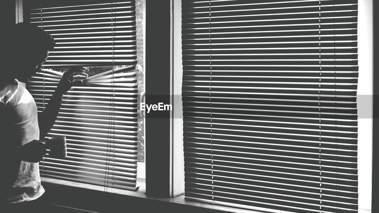 Man peeking through window blinds at home