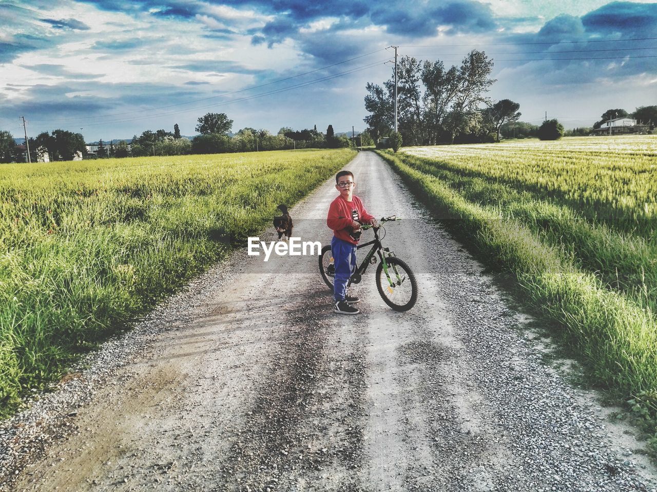 MAN RIDING MOTORCYCLE ON ROAD AMIDST FIELD AGAINST SKY