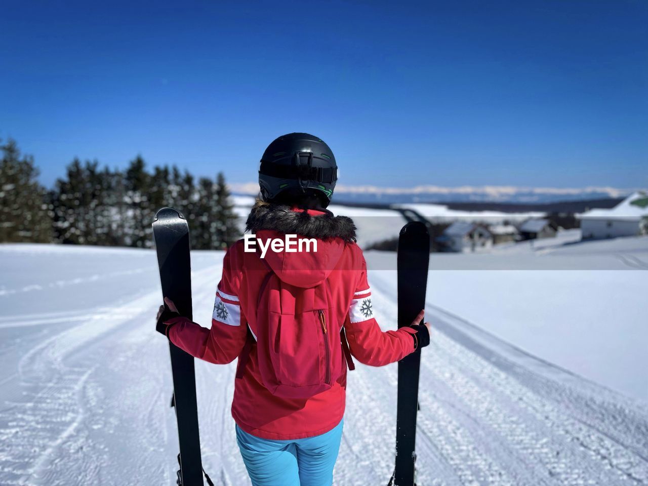 Rear view of woman skier standing on the slope and holding her skis in a vertical position