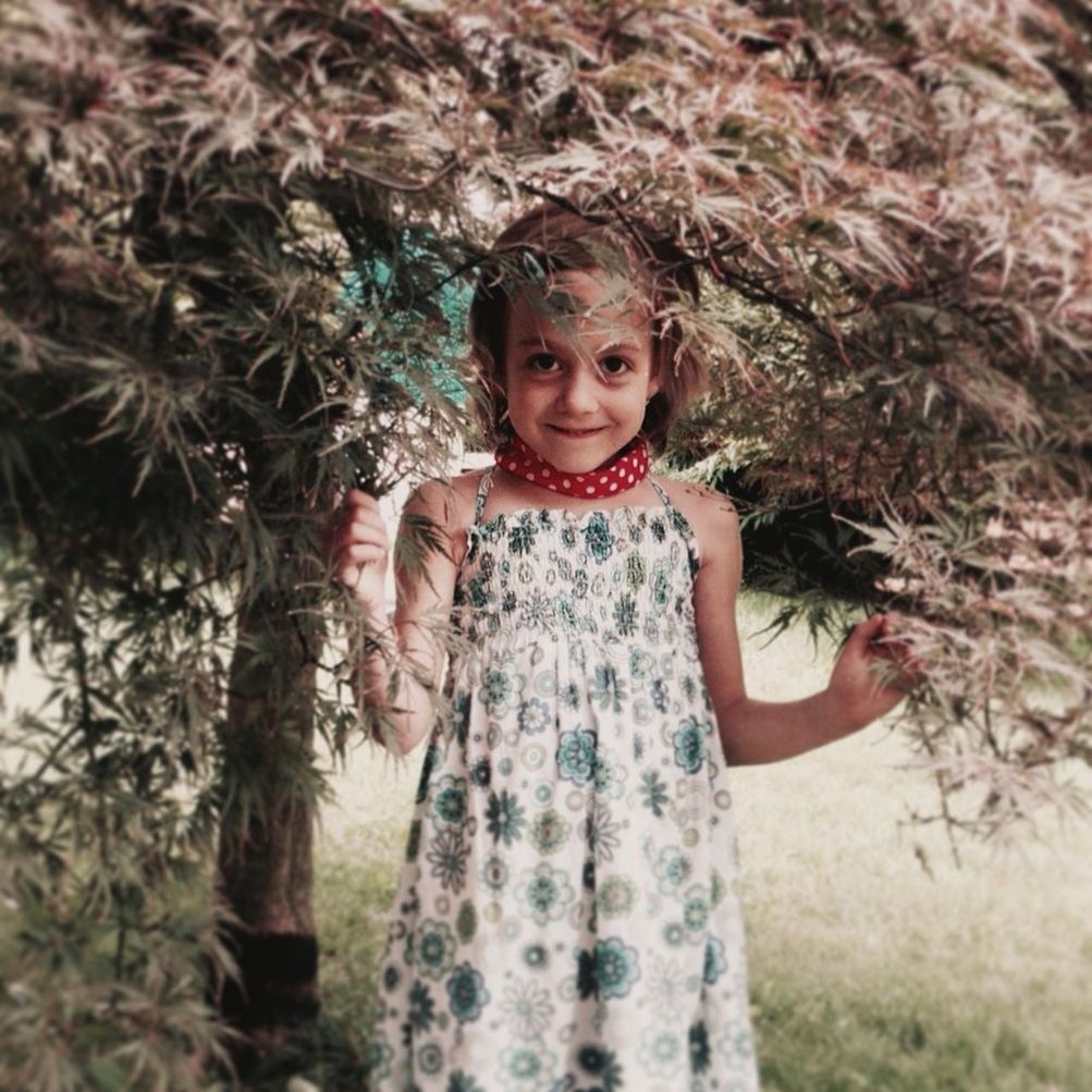 PORTRAIT OF SMILING GIRL STANDING AGAINST PLANTS