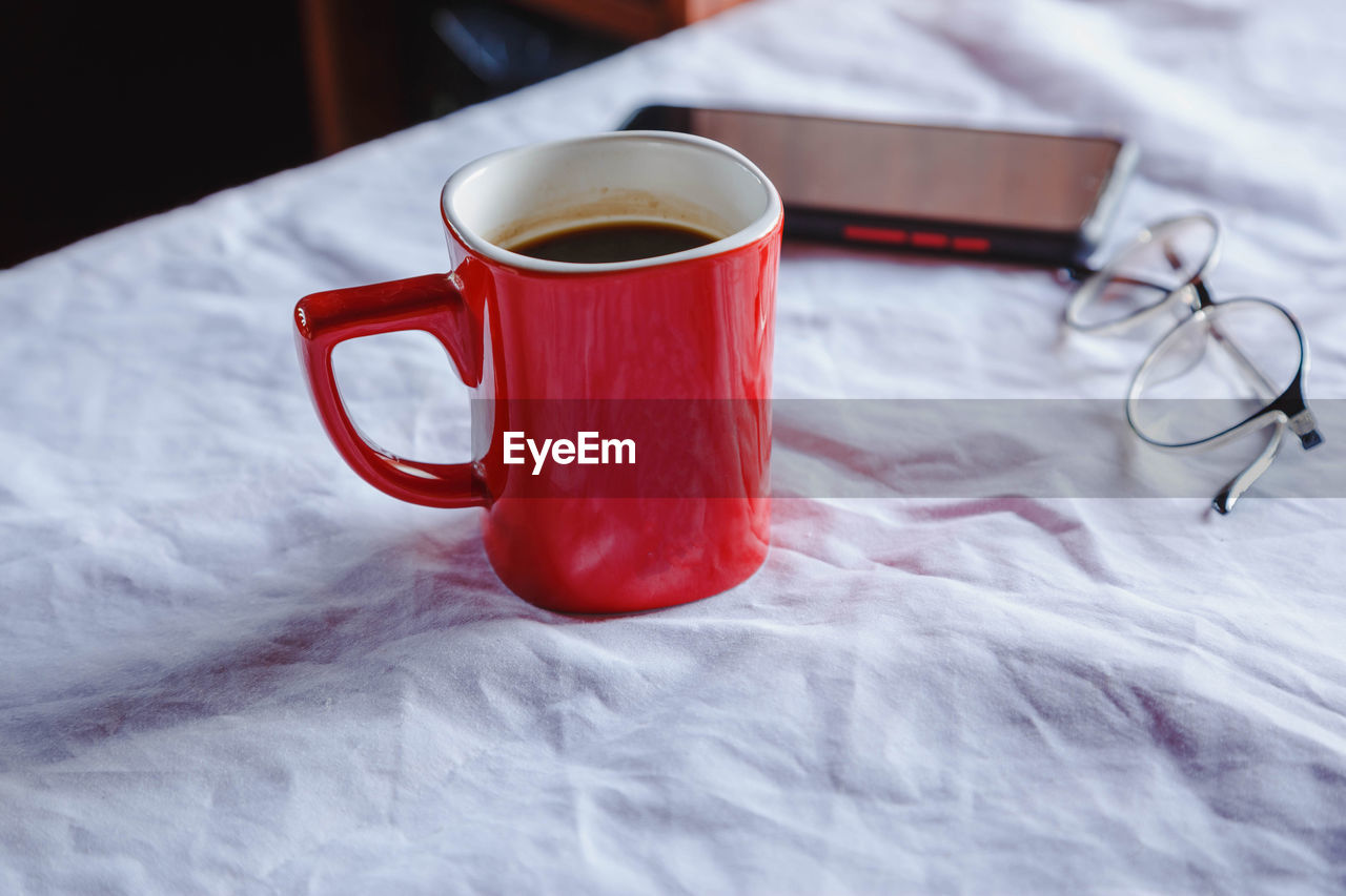 CLOSE-UP OF CUP OF COFFEE ON TABLE WITH BED