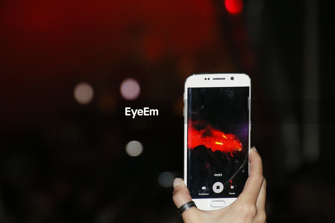 Cropped hand of woman photographing illuminated red stage at night