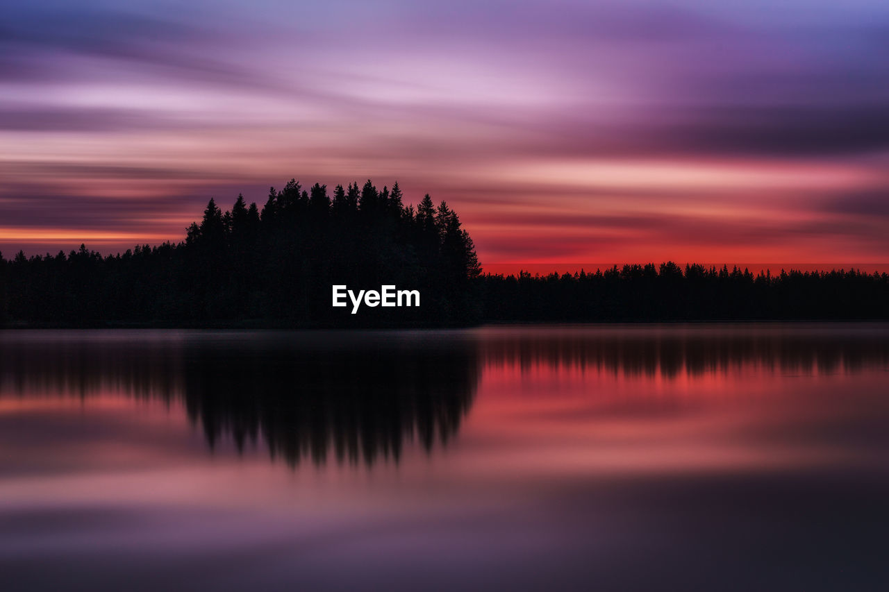 Silhouette trees by lake against sky during sunset