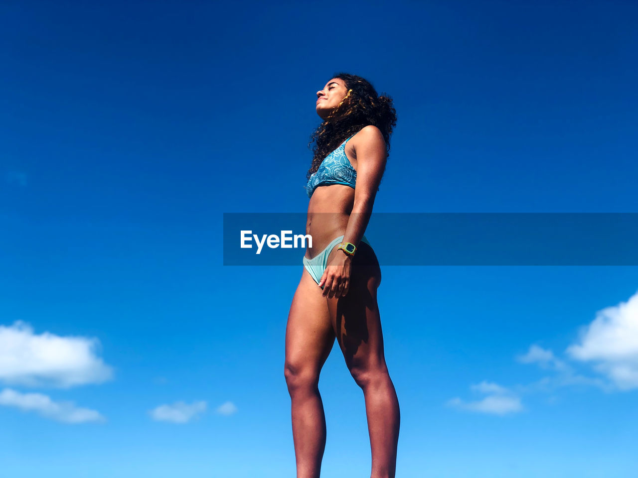 Low angle view of woman in bikini standing against blue sky