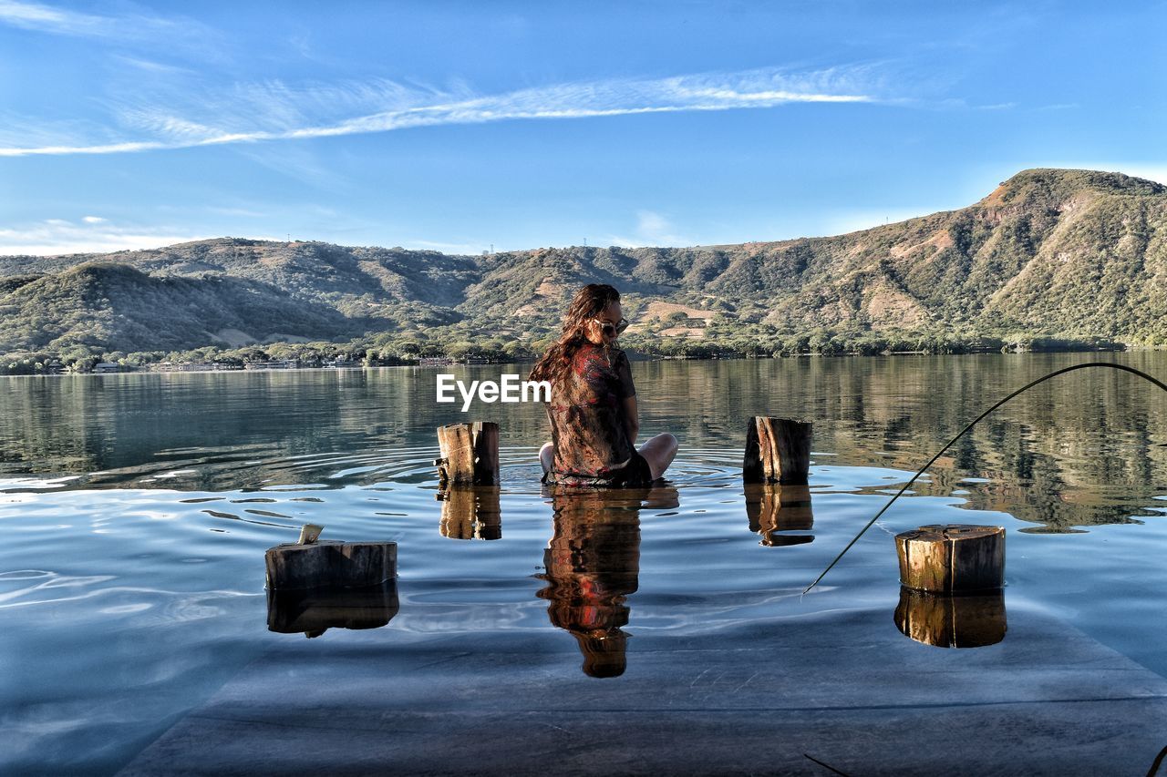 Woman sitting amidst lake on wood