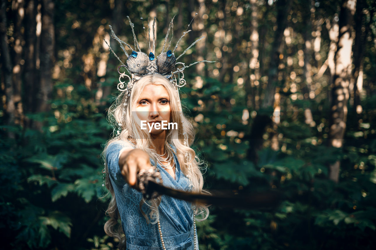 Portrait of young woman standing against trees