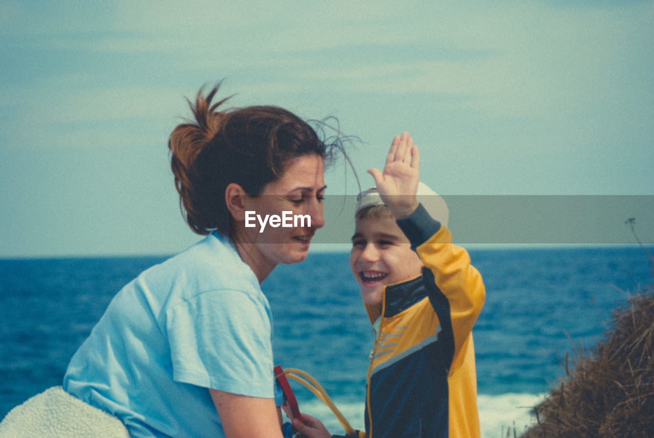 Side view of mother and son standing at beach against sky