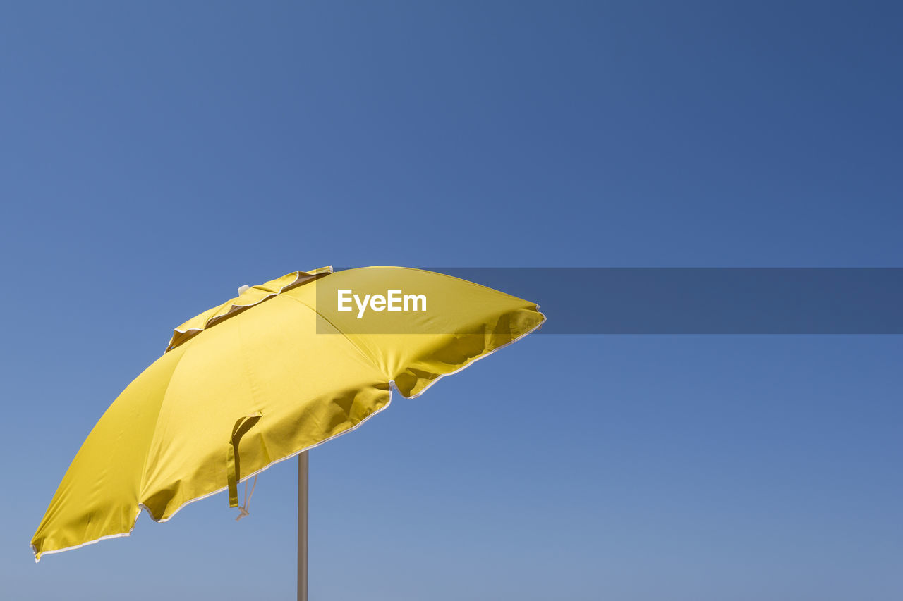 Low angle view of yellow umbrella against clear blue sky