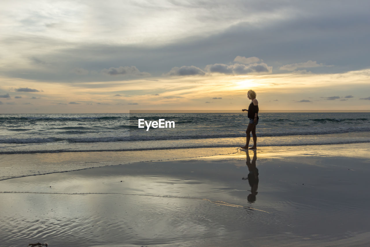 Woman standing on beach against sky during sunset