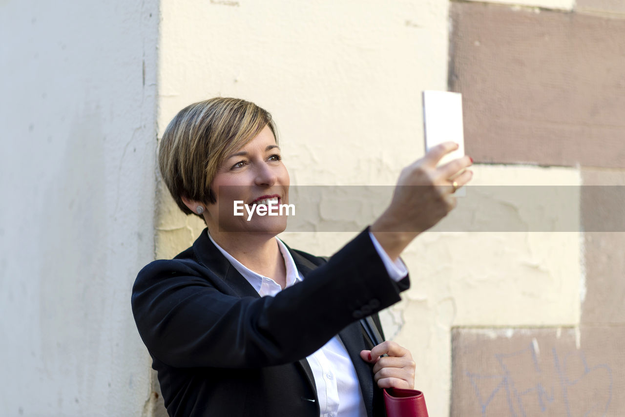 portrait of businessman using mobile phone against wall