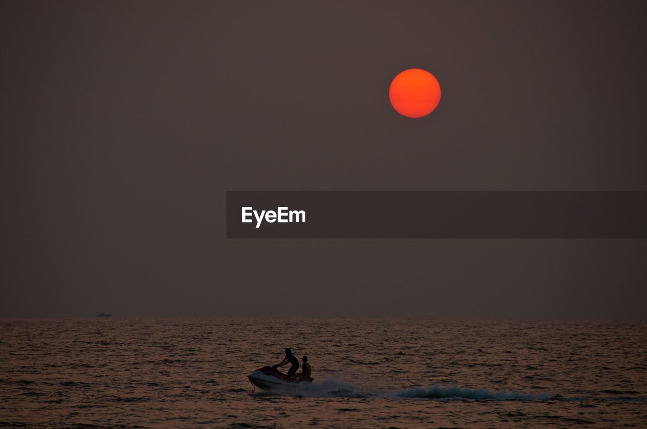 People jet boating in sea against sky during dusk