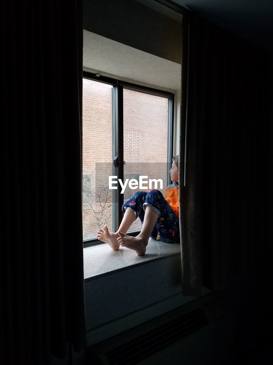 Full length of boy sitting by window at home