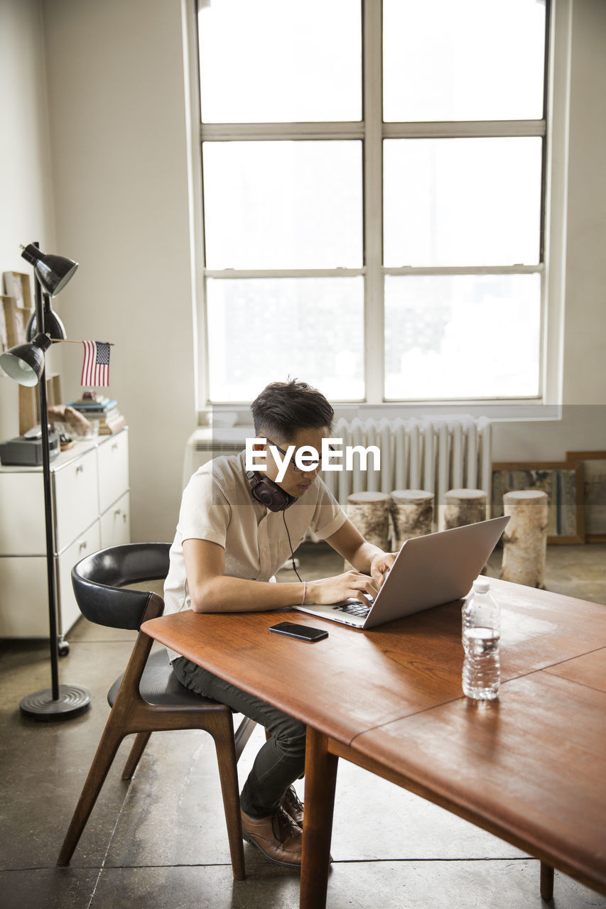 Businessman wearing headphones using laptop at table in creative office