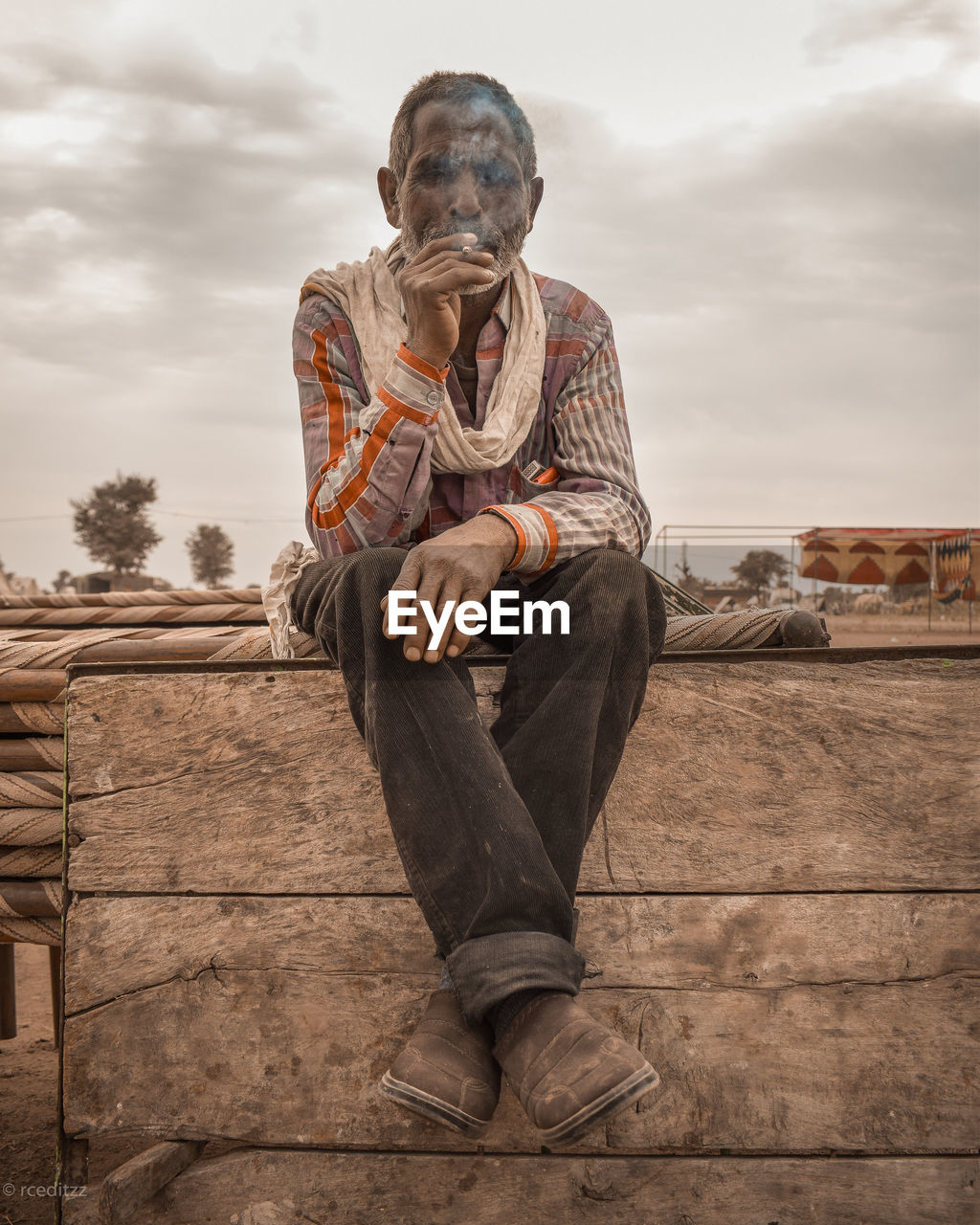 Smoking man sitting on wood against sky