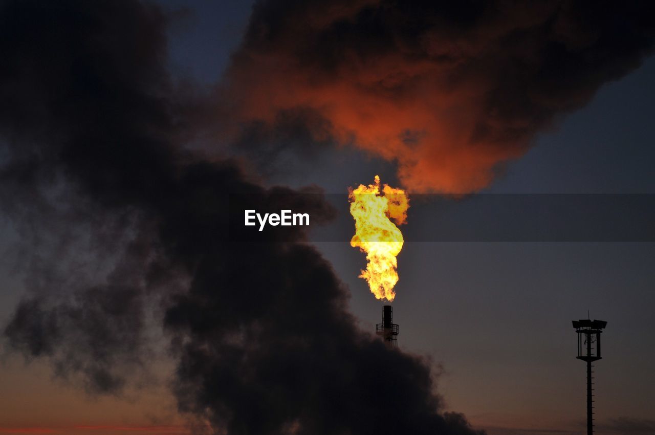 Low angle view of fire emitting from smoke stack against sky during sunset