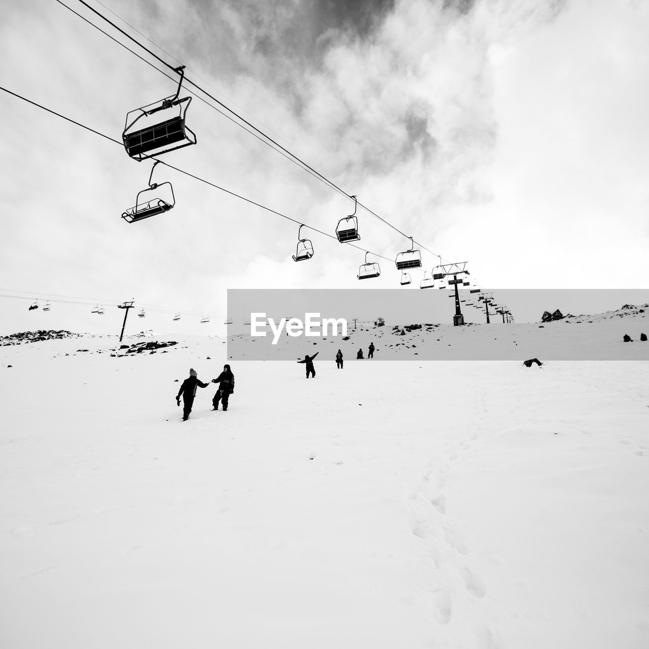 People under ski lift on snowcapped mountain against sky