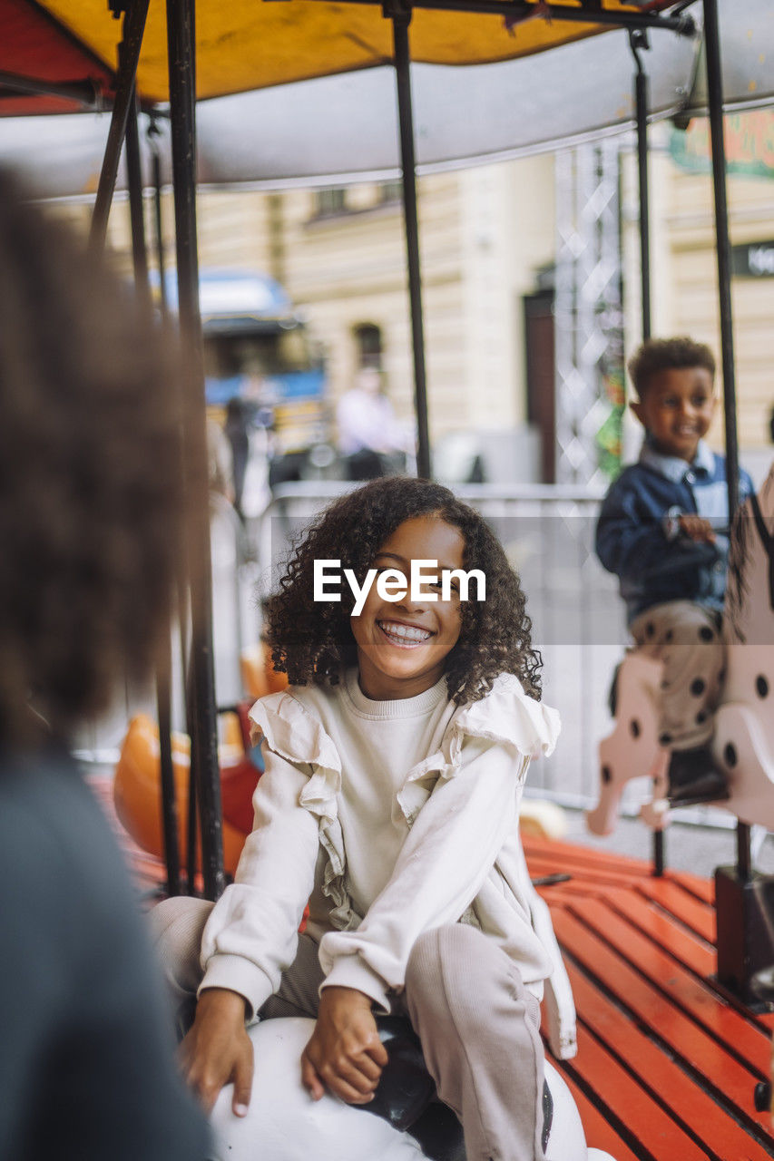 Portrait of smiling girl with curly hair enjoying during ride on carousel at amusement park