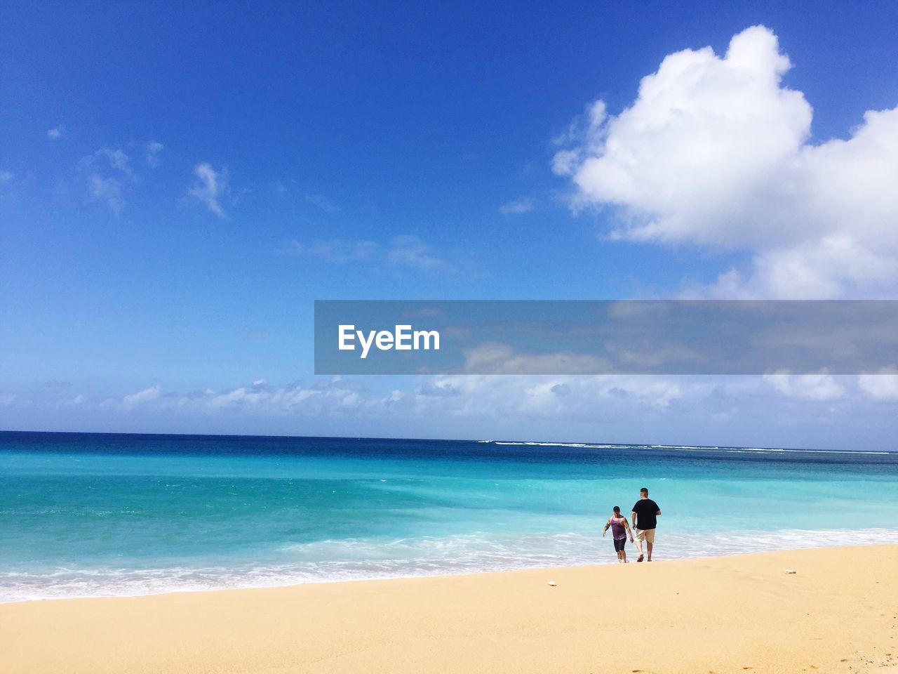 Men walking on shore at beach against blue sky