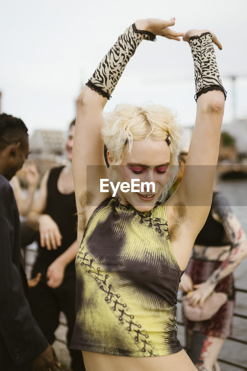 Carefree non-binary person showing armpit hair with friends in background