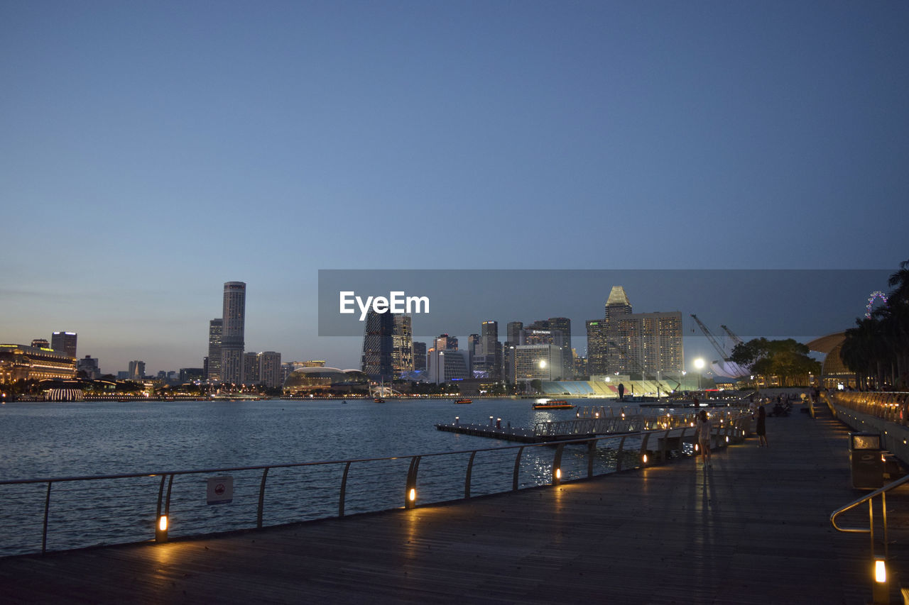 ILLUMINATED CITY BUILDINGS BY RIVER AGAINST SKY