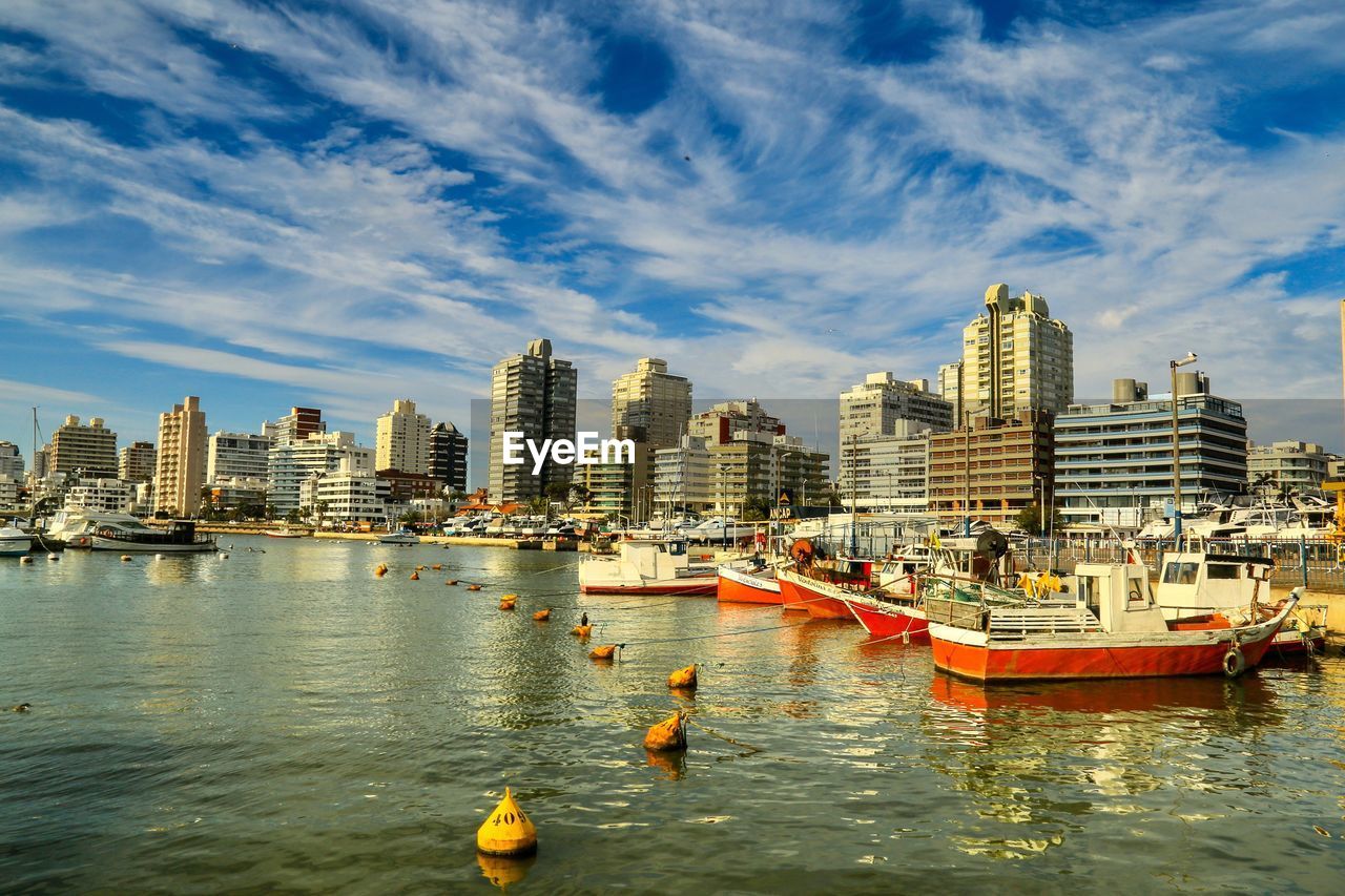 Boats in sea by cityscape against sky