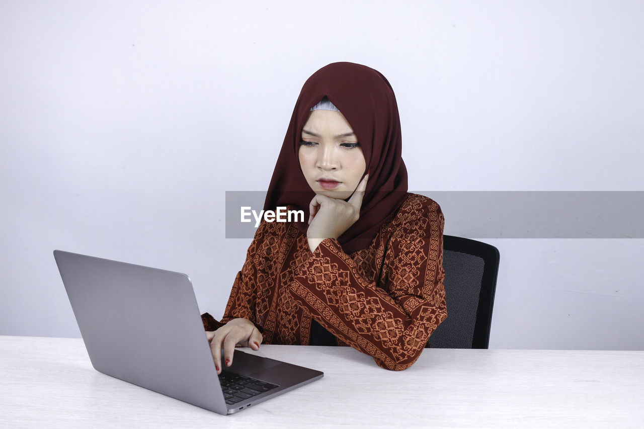 WOMAN LOOKING AT CAMERA WHILE SITTING ON LAPTOP