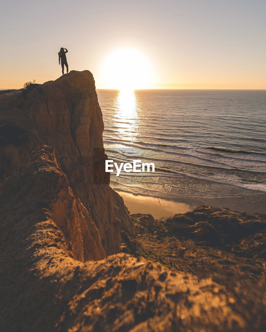 Woman standing on cliff against sea during sunset