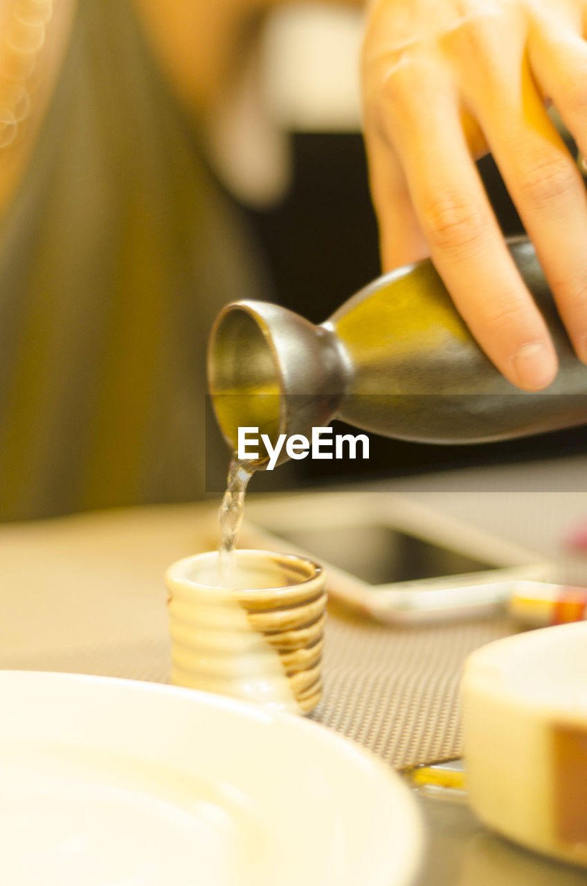 Cropped image of hand pouring hot sake from traditional flask