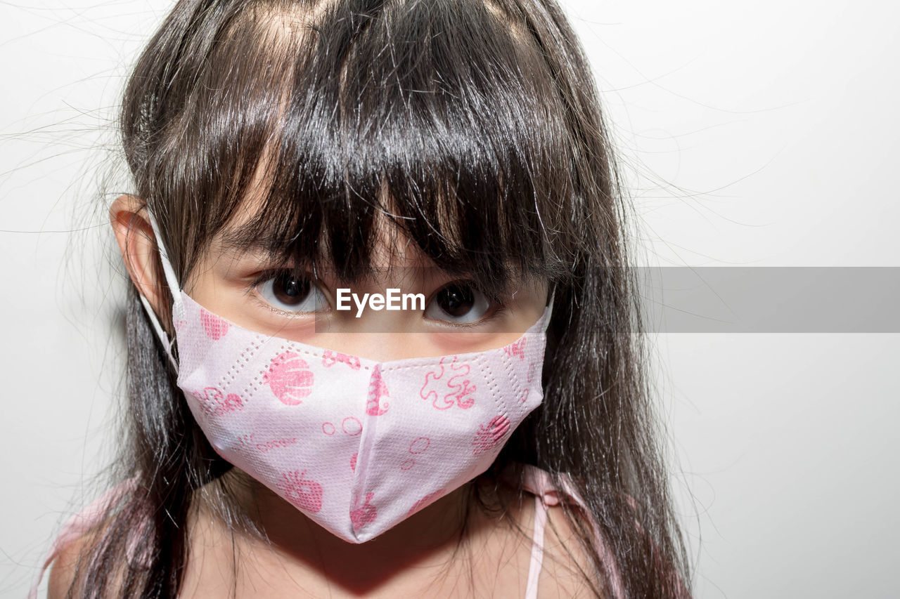 Close-up portrait of girl wearing mask against white background
