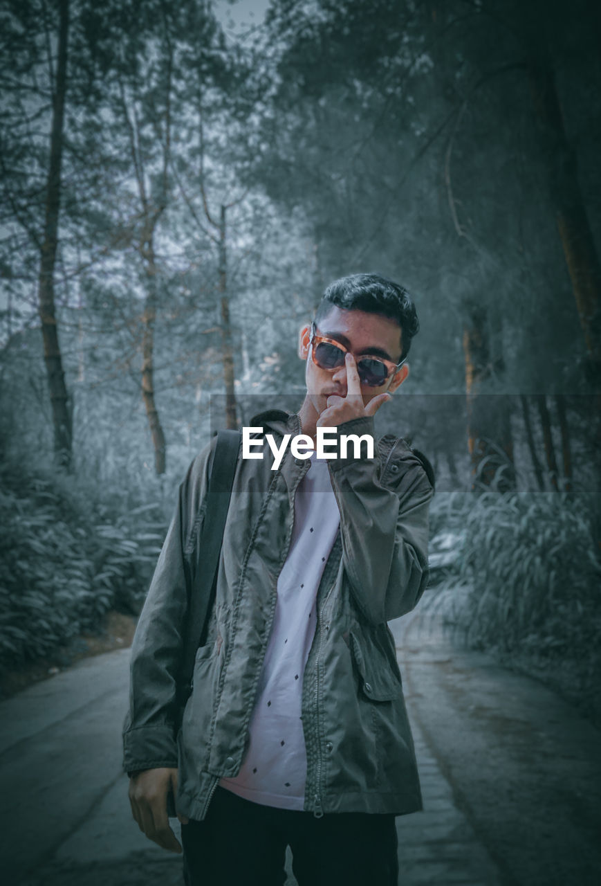 Young man wearing sunglasses standing against trees