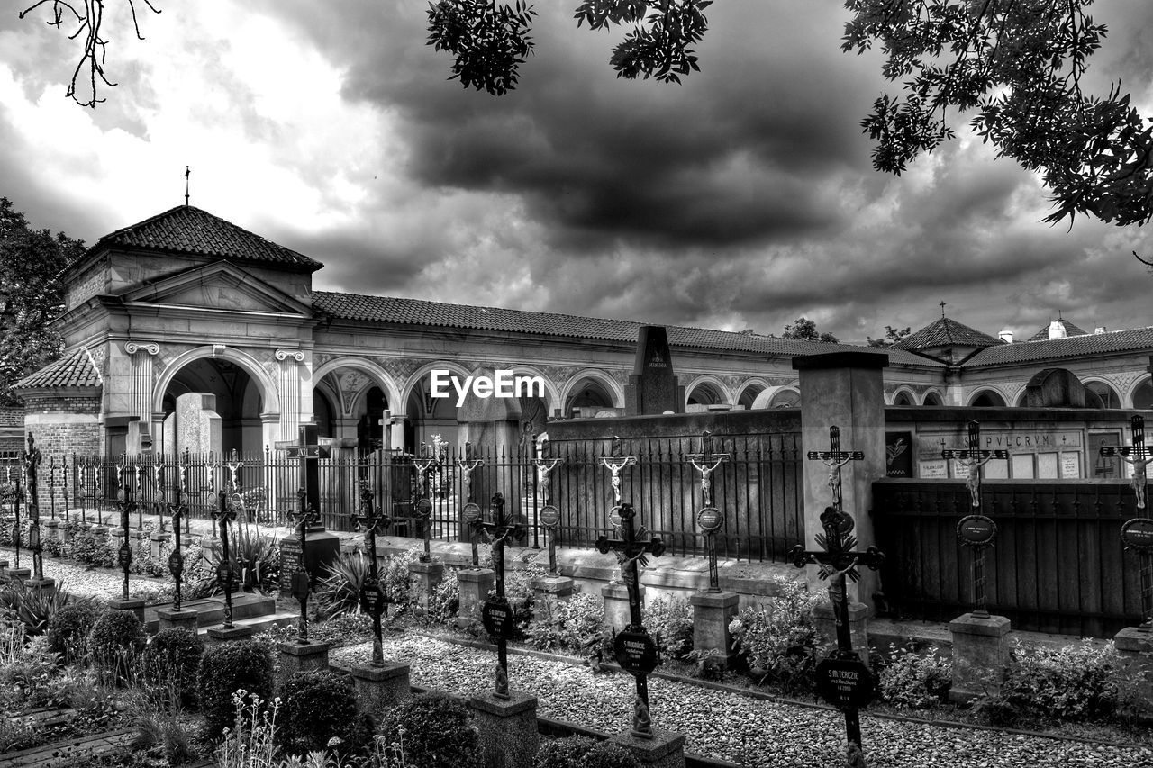 Exterior of church by cemetery against cloudy sky