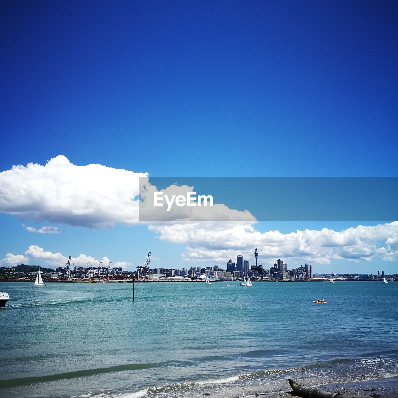 VIEW OF CITY AT WATERFRONT AGAINST CLOUDY SKY