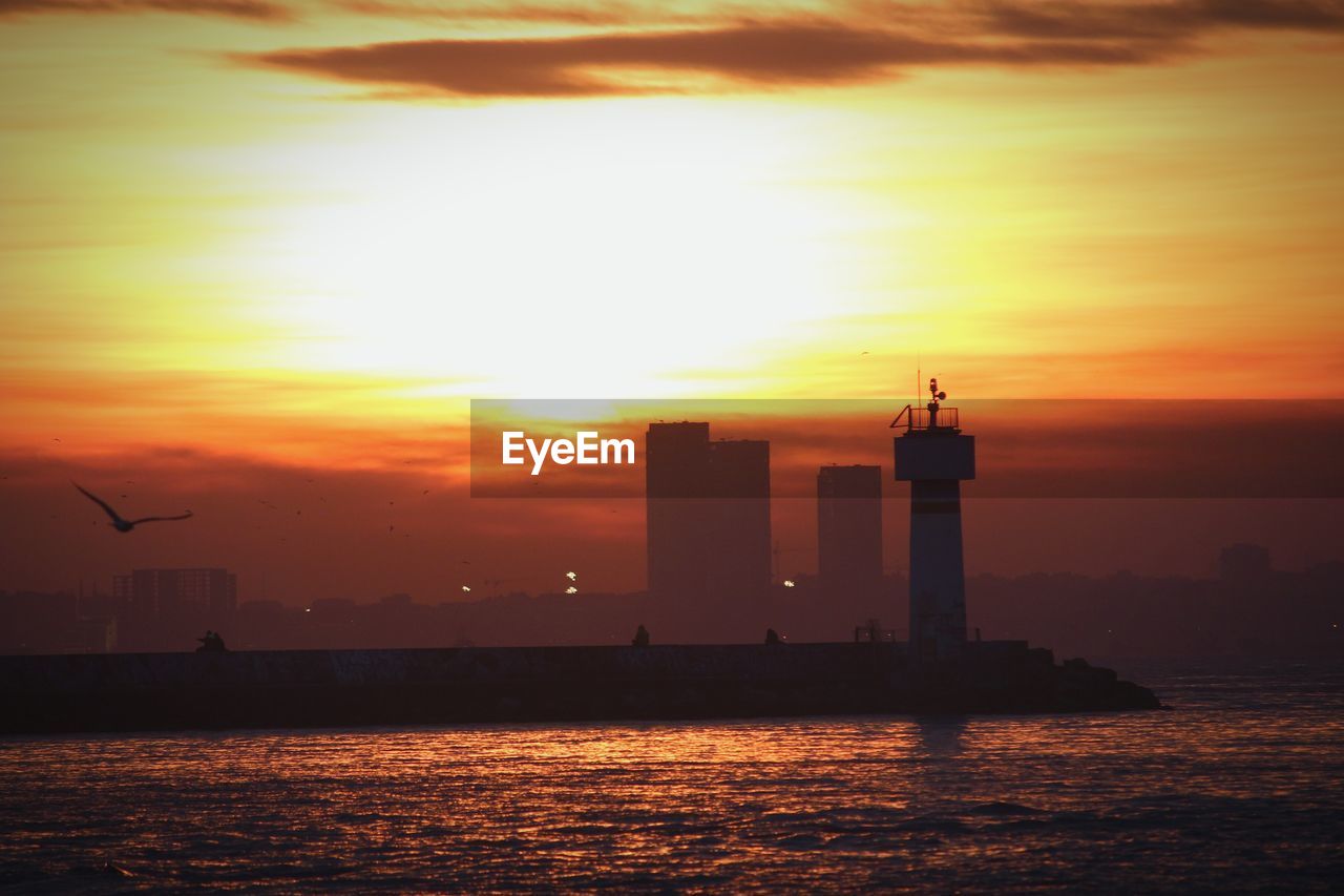 Silhouette lighthouse by sea against sky during sunset