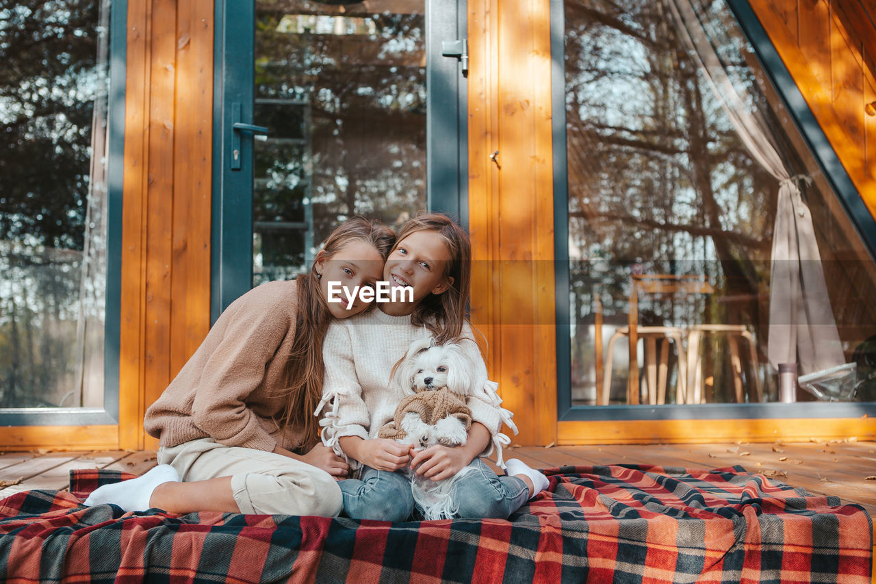 Portrait of cute sisters with dog sitting outdoors