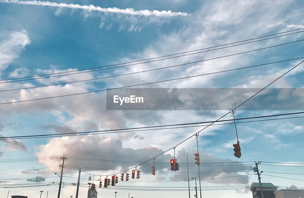 Low angle view of stoplights hanging against cloudy sky